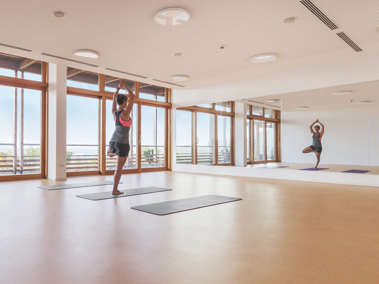 Frau macht Yogapose im lichtdurchfluteten Fitnessstudio des Wellnesshotels in Bayern